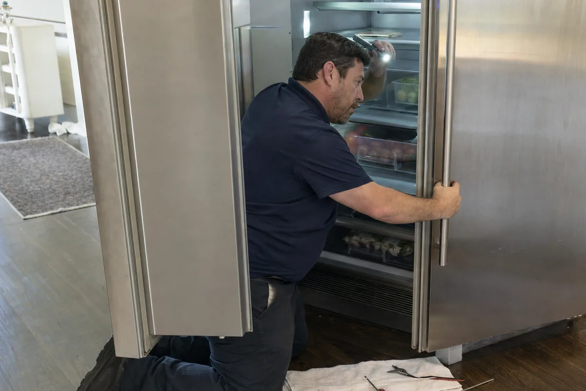 A stainless built-in refrigerator standing open in a kitchen, shelves and drawers exposed, a work towel spread on the floor